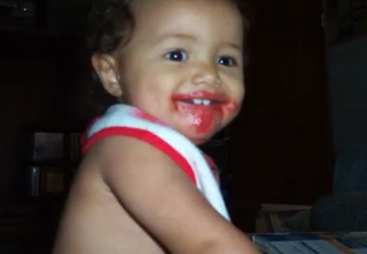 Little baby wearing white and red bib smiling with icing all over face